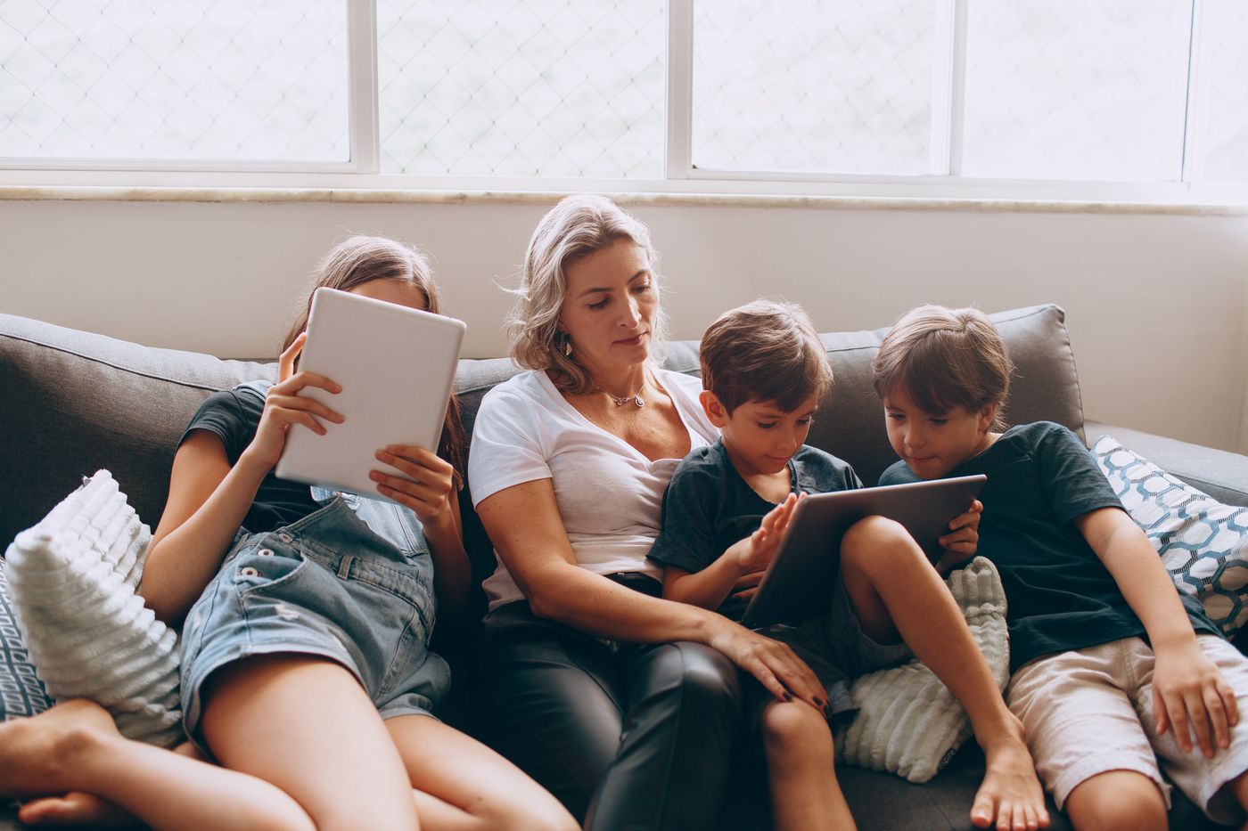 Mãe e filhos reunidos no sofá usando tablets